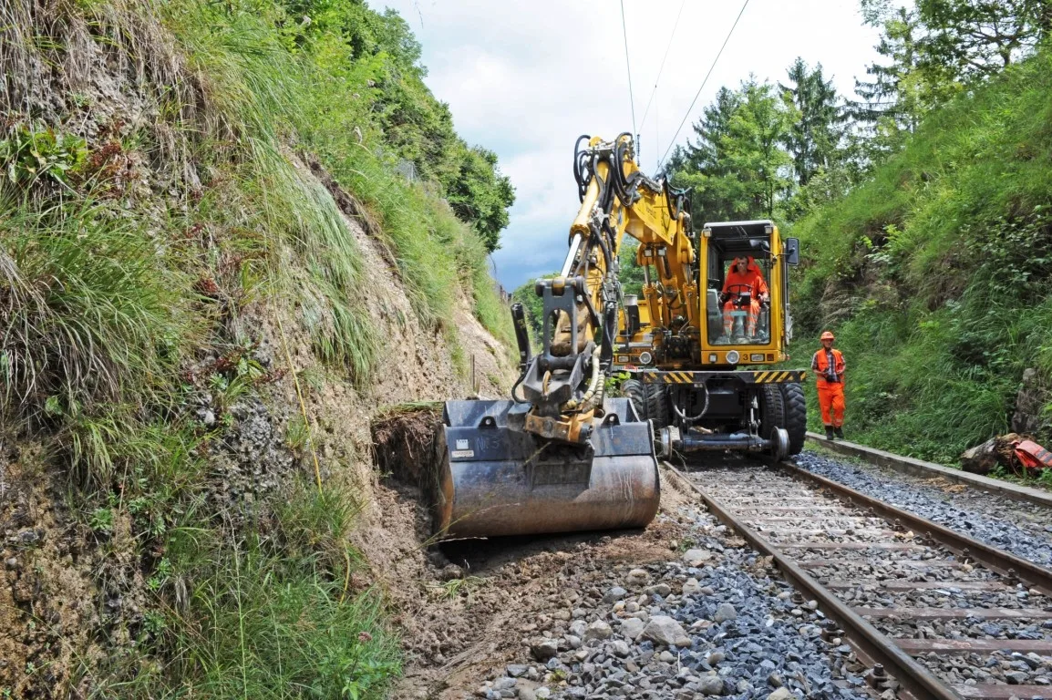 Gleisbagger schaufelt Dreck von einem Bahngleis.
